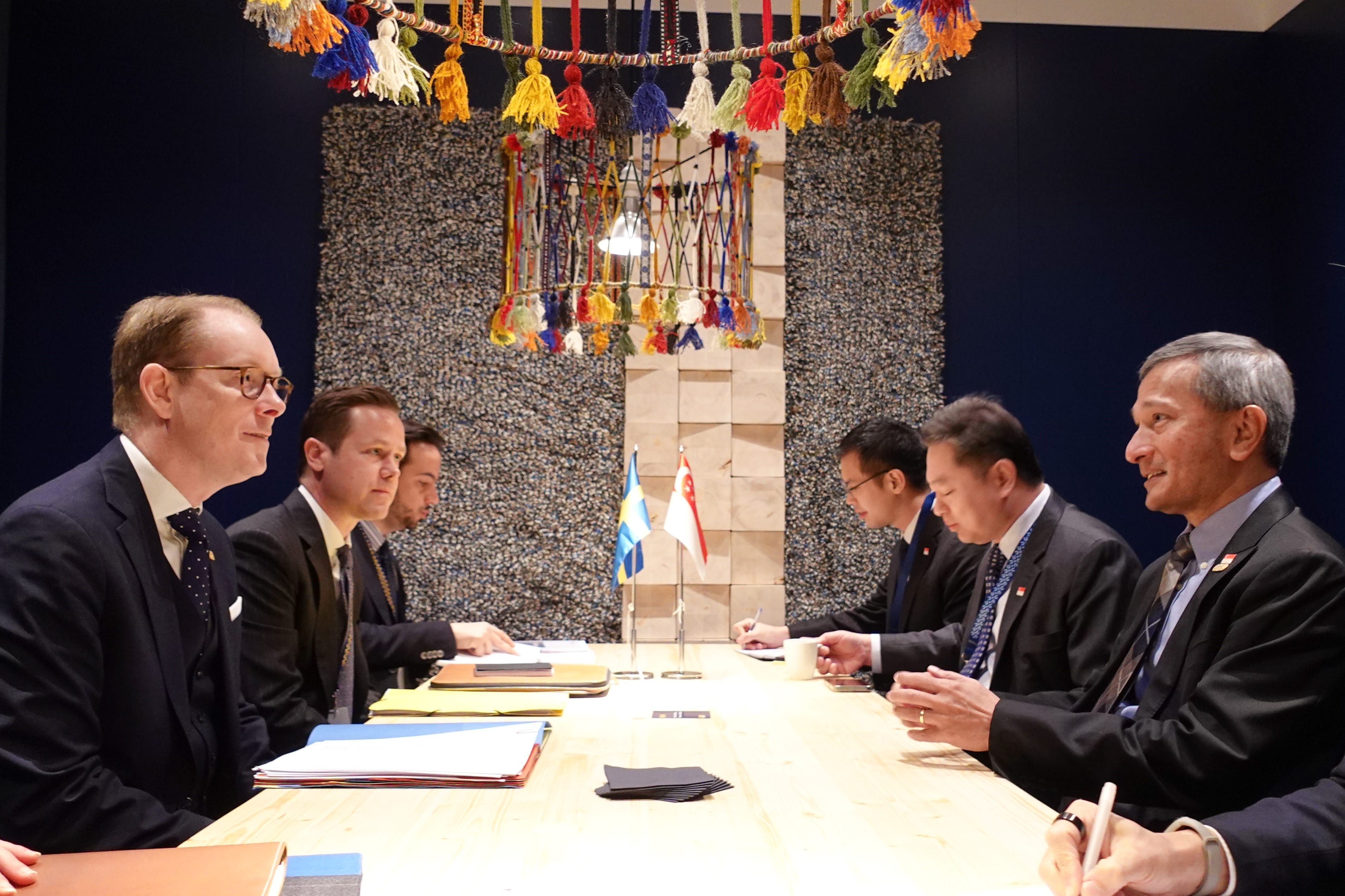 Government officials at a table with Sweden and Singapore flags, signing documents.